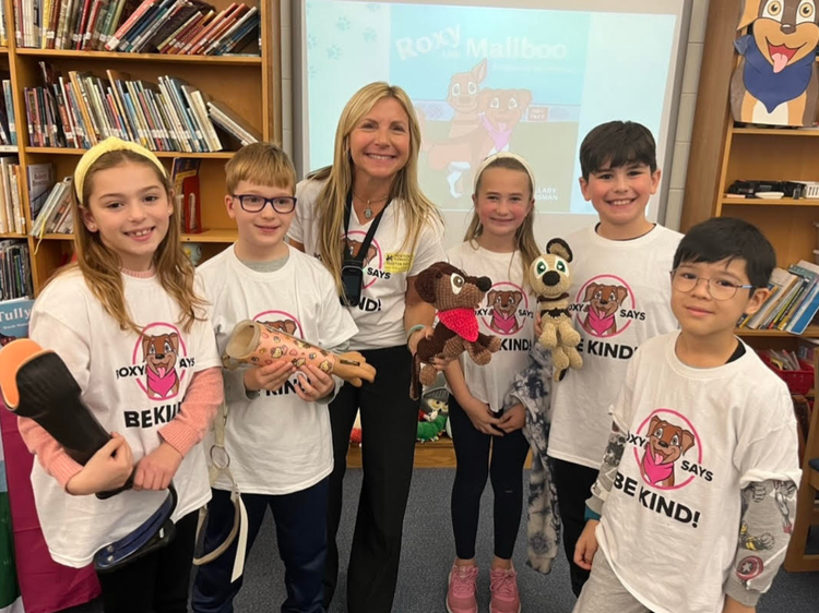 Group of children and author of the Adventures of Roxy, Hillary Sussman in a classroom setting with 'Be Kind' t-shirts and Roxy stuffed animals.