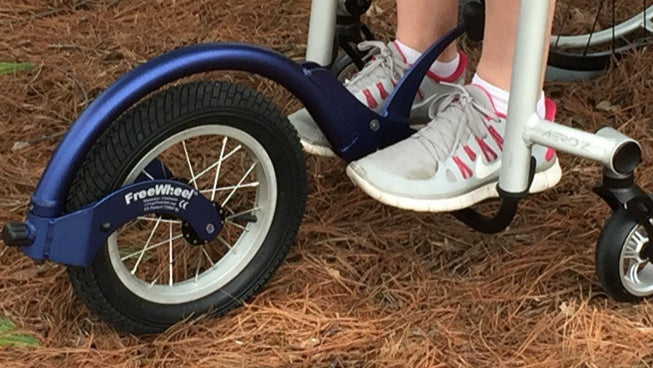 Detail of a FreeWheel Wheelchair Attachment Blue on a wheelchair outdoors.