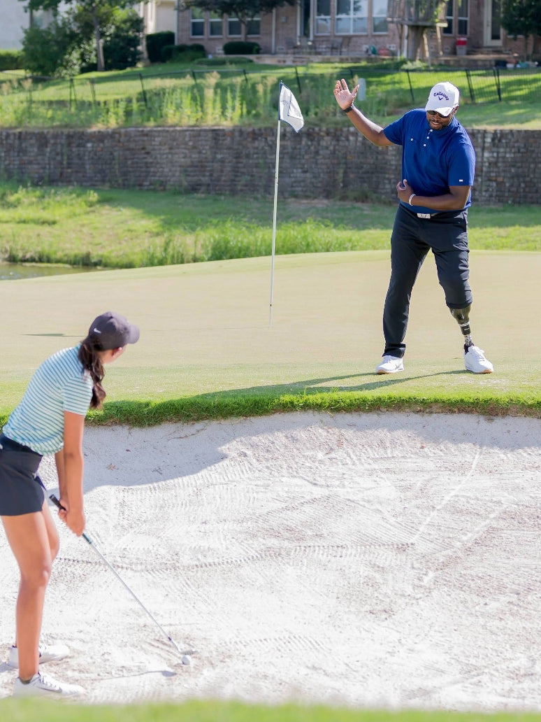 Carlos Brown coaching a golfer that's in a bunker.