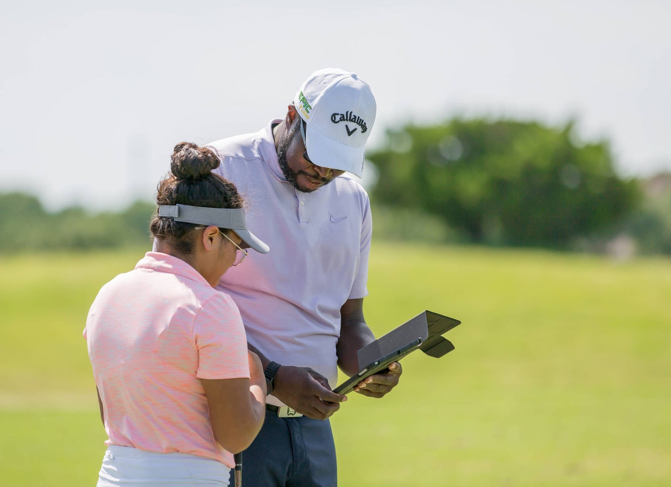 Carlos Brown watching a golf swing on a tablet with a golfer.