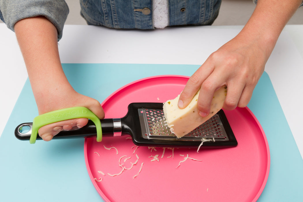 Person using an EaZyHold with a grater to shred cheese on a pink plate with a blue background