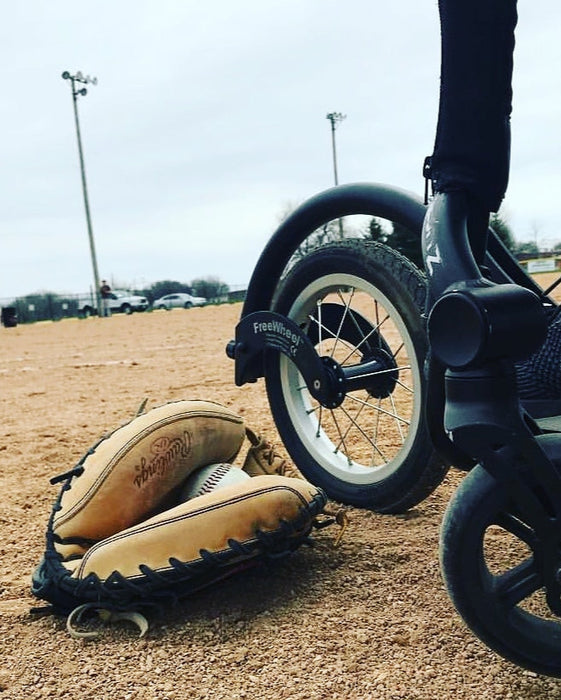 Detail of a FreeWheel Wheelchair Attachment Black on a wheelchair on a baseball field.