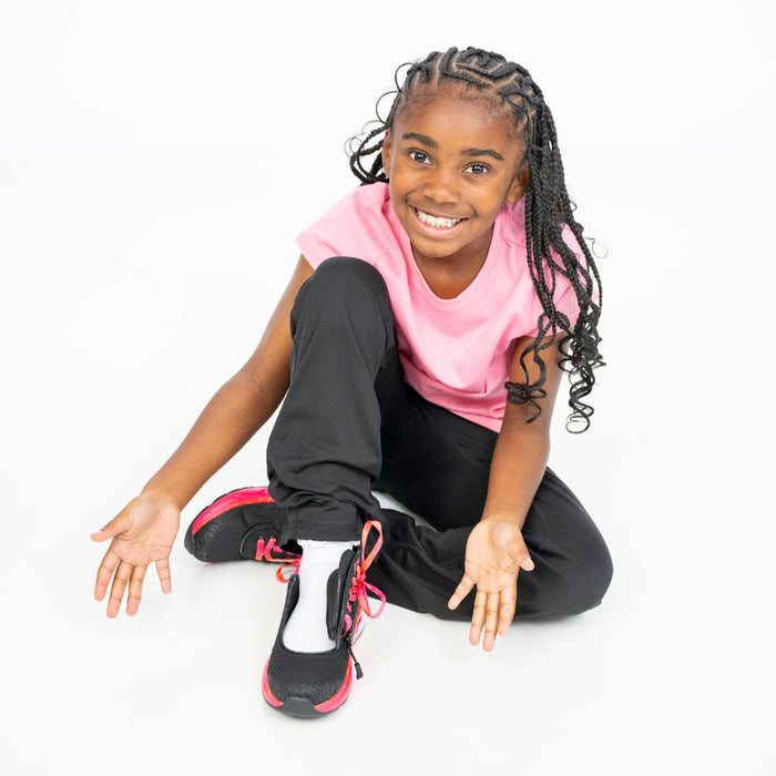 Young girl sitting on the floor wearing a pink shirt and black pants modeling the  Black/Fuchsia Fire BILLY Sport Inclusion with the top open on a white background