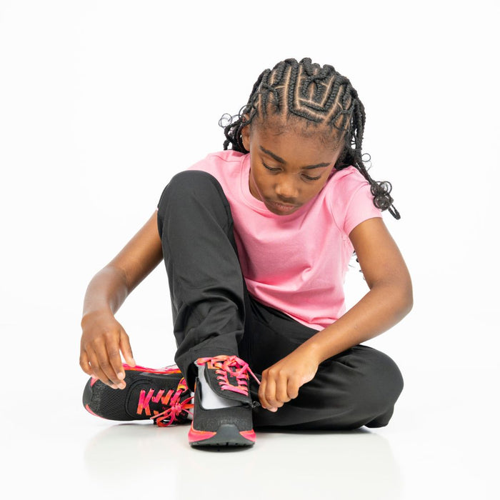 Young girl sitting on the floor wearing a pink shirt and black pants modeling the  Black/Fuchsia Fire BILLY Sport Inclusion zipping the top open on a white background