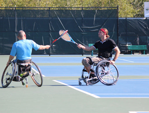 Two GLASA wheelchair tennis athletes greeting each other by touching the sides of their tennis racquets together.