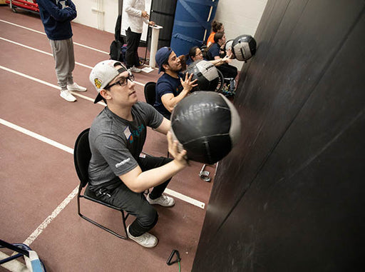 5 GLASA Athletes throwing medicine balls against a wall while sitting in a chair.