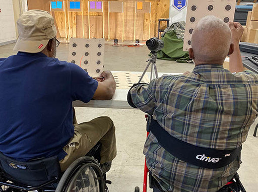 Two GLASA athletes using wheelchairs looking at a target that they shot with air rifles.