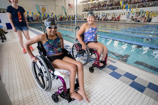 Two GLASA athletes using a wheelchair getting ready to race at a swim meet.
