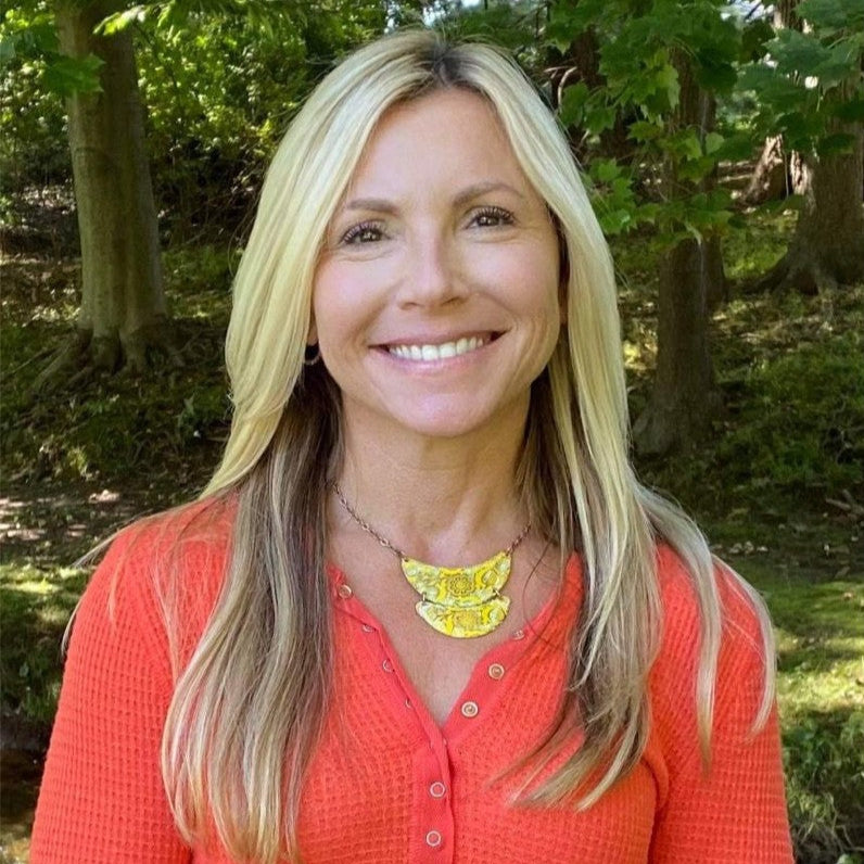 Portrait of Hillary Sussman. She is wearing an orange shirt and yellow necklace outdoors.