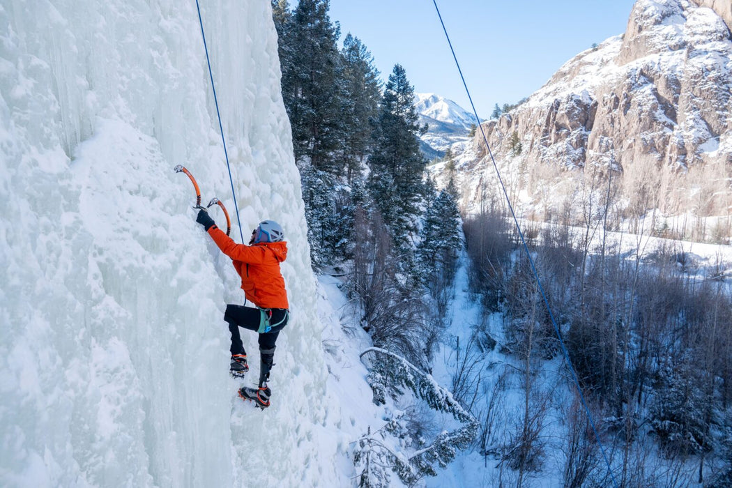 Person ice climbing a frozen waterfall with a snowy mountain landscape in the background