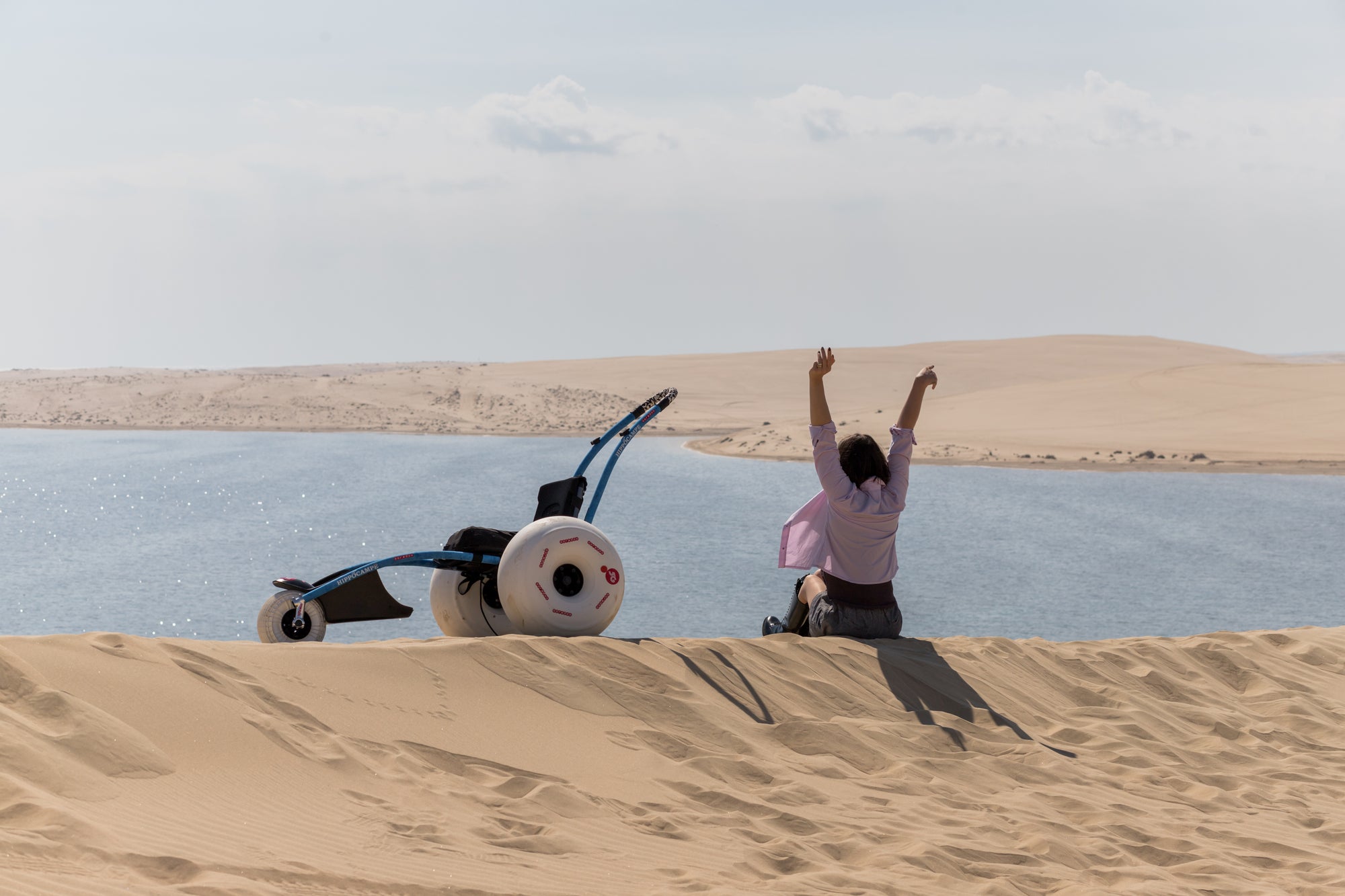 Person with arms raised on a sand dune overlooking a lake.