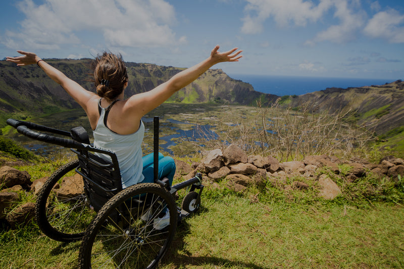 Person in a wheelchair with arms outstretched overlooking Easter Island.