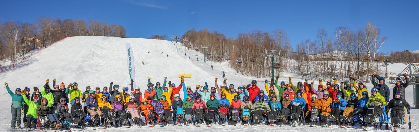 Group portrait of Green Mountain Adaptive Sports in colorful winter clothing on a snowy slope with a clear blue sky.