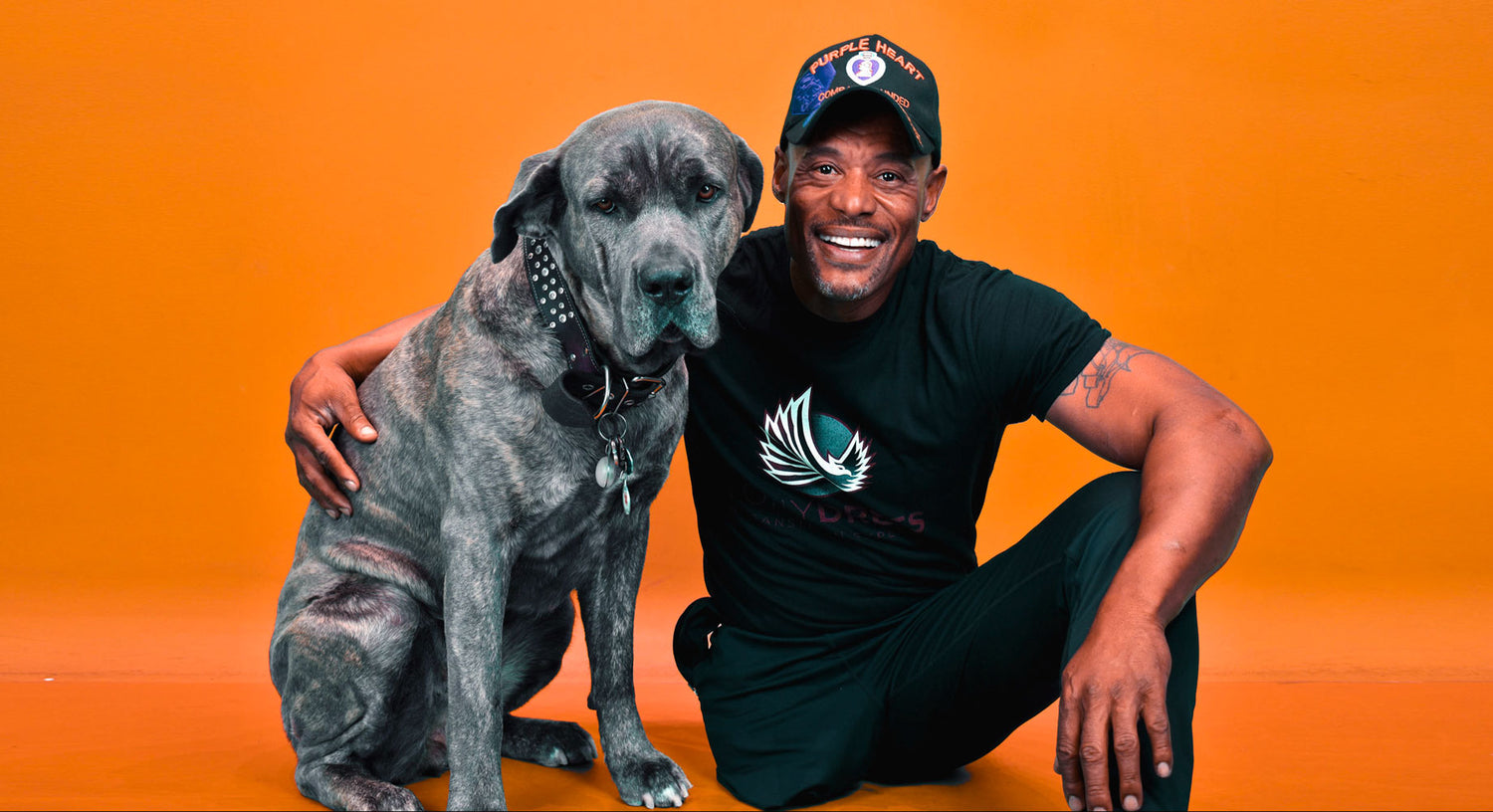 AMPLIFE SUPPORTER TONY DREES SMILING WITH HIS DOG AGAINST AN ORANGE BACKGROUND