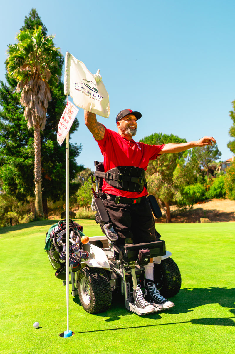 Candid photo of Amplife® Foundation & Amplife® Founder Abdul Nevarez celebrating and holding the flag on his 1st one-armed hole-in-one as a right above knee amputee with severe nerve damage in his left arm and left leg in an adaptive golf cart at Canyon Lakes 5th