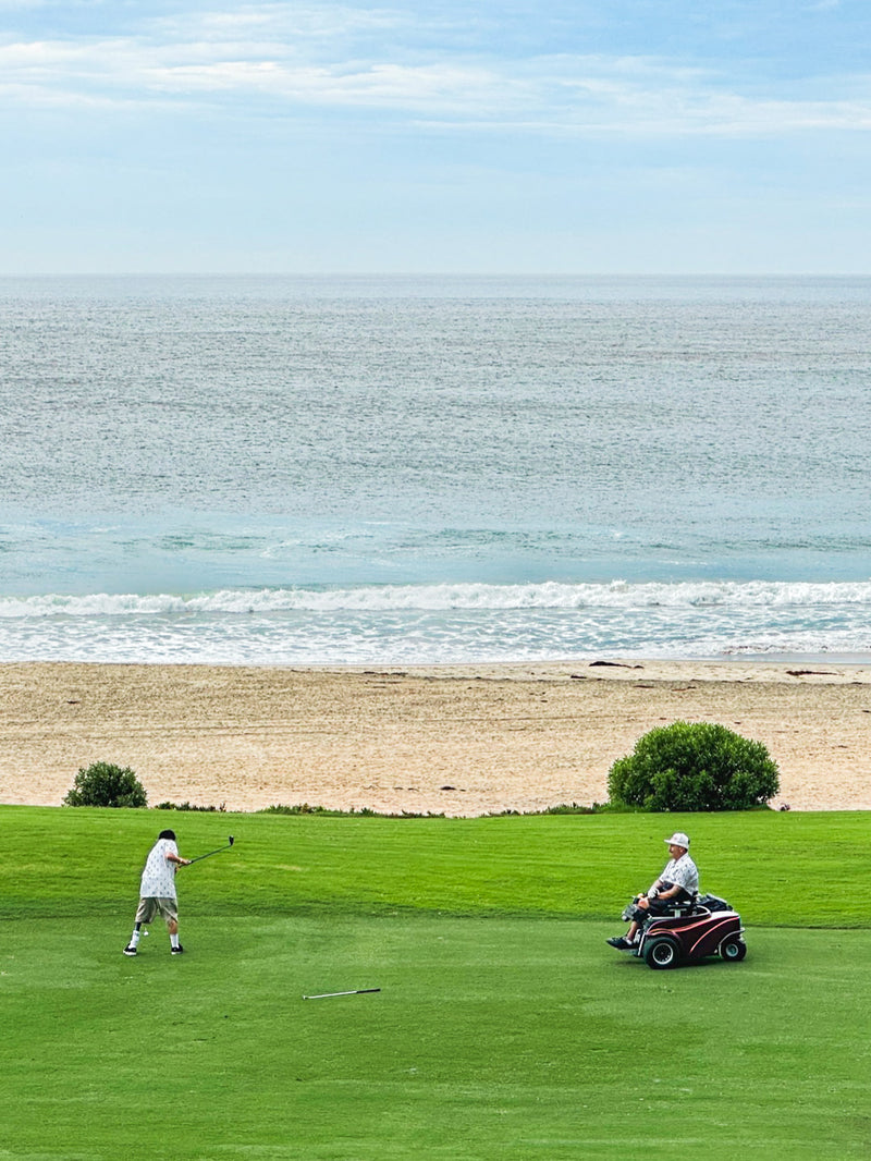 Two golfers on a coastal fairway wearing Amplife® Clothing getting ready to chip.