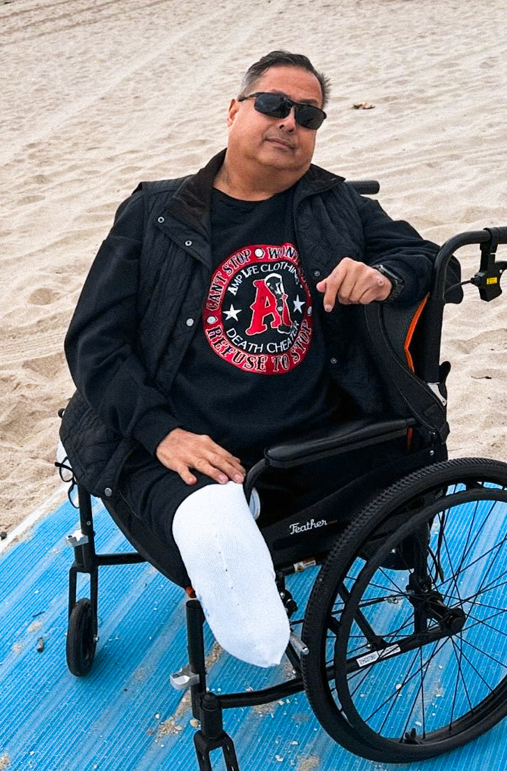 Team Amplife® Ambassador Bert Chirino wearing the Amplife Death Cheater Crewneck Sweatshirt while sitting in his wheelchair on the beach