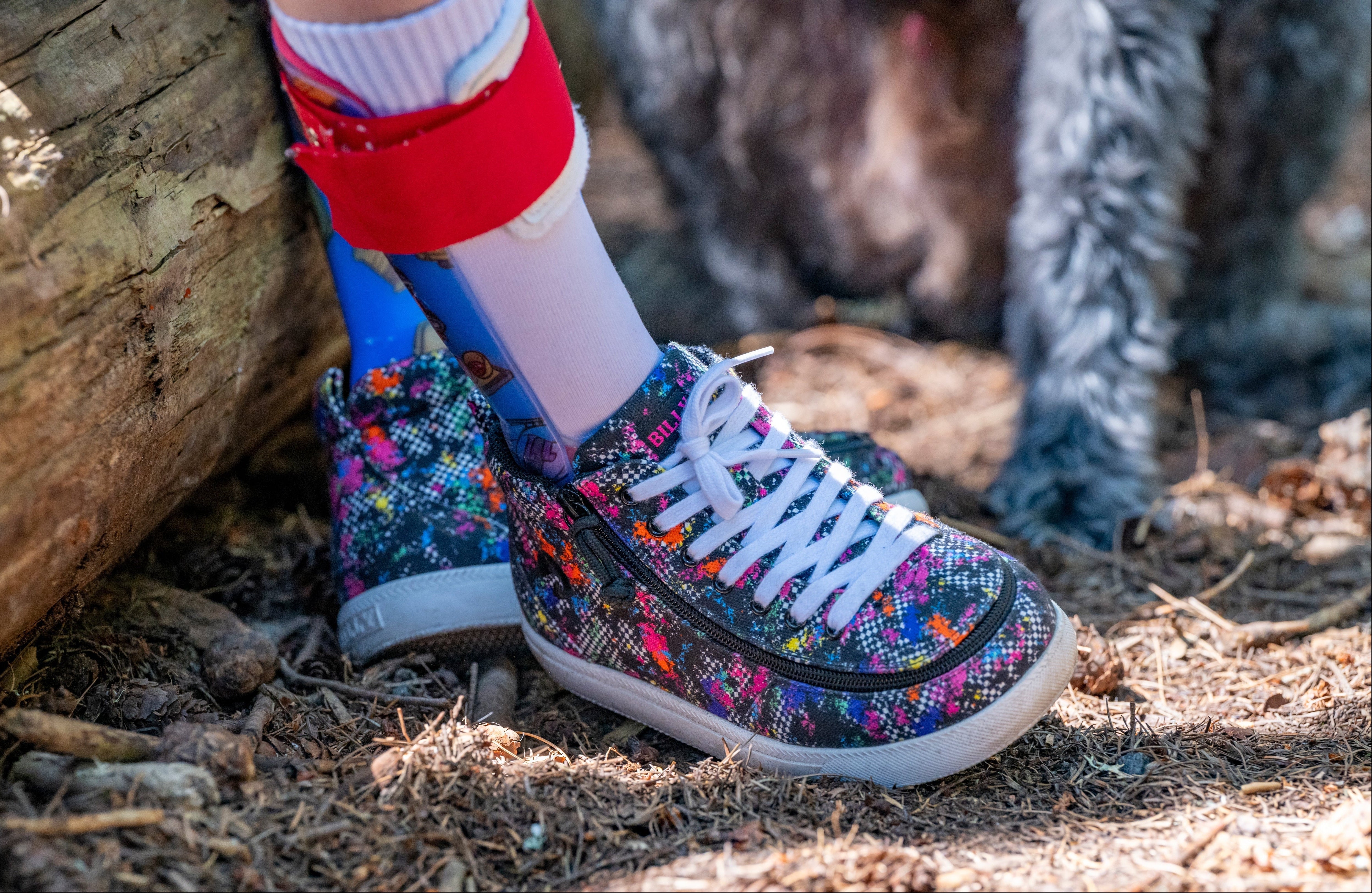 Colorful patterned BILLY Footwear worn with a red AFO, standing on a natural ground.
