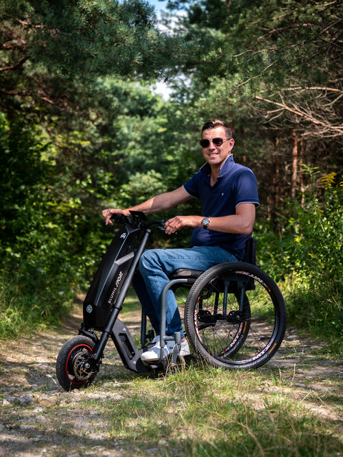 Man riding the Blumil Sport Electric Wheelchair Attachment in a forested area.
