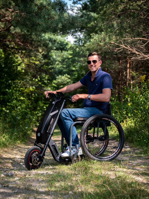 Man riding the Blumil Sport Electric Wheelchair Attachment in a forested area.