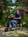 Man riding the Blumil Sport Electric Wheelchair Attachment in a forested area.