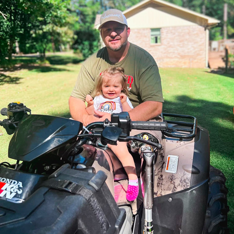 Team Amplife® Ambassador Christopher Scott Ashley sitting on a large ATV with a baby in his lap while wearing the Severed Society Drip® T-Shirt