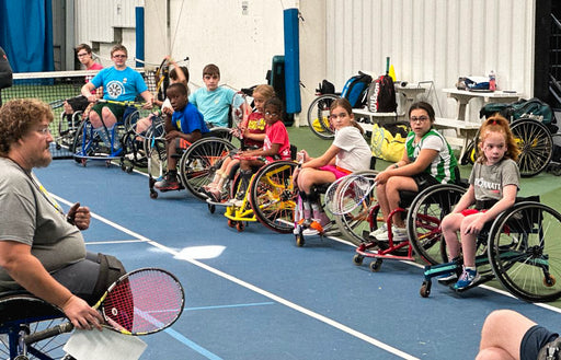 Group of intro to wheelchair tennis participants listening to their coach on an indoor court.