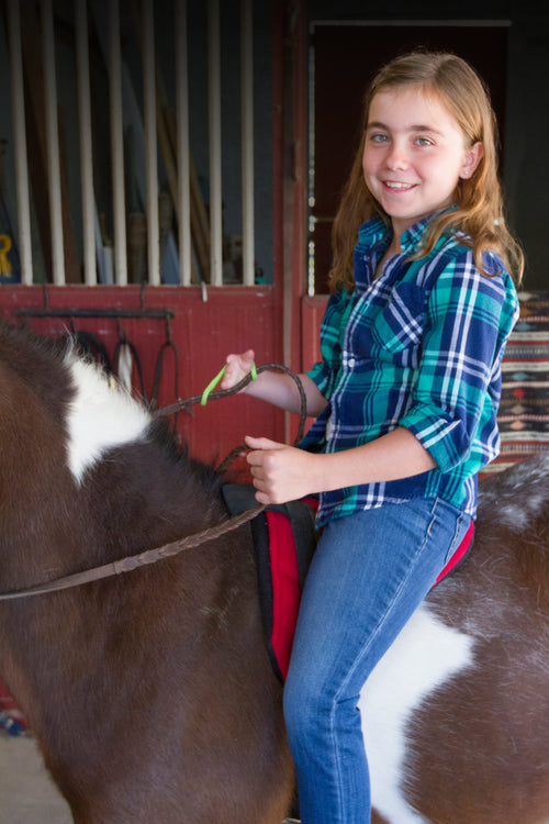 Girl sitting on a horse in a stable using an EaZyHold grip aid.