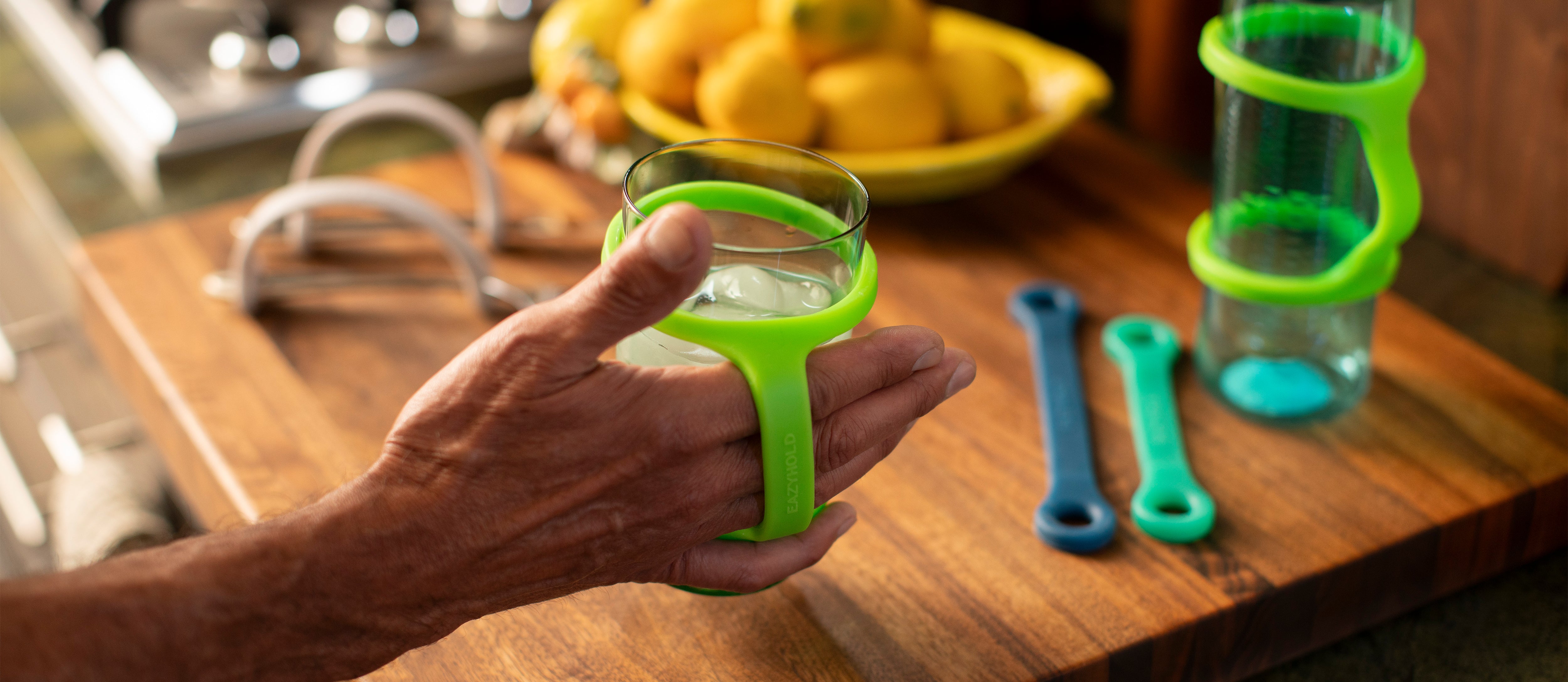 Person holding a glass with an EaZyHold, surrounded by kitchen items on a wooden surface.