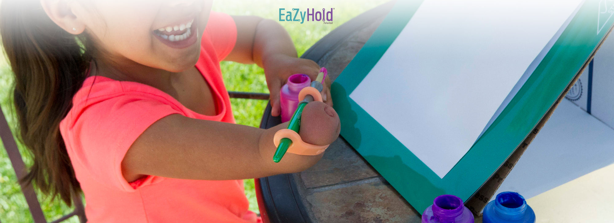 Child using a paintbrush with EazyHold product on a whiteboard outdoors