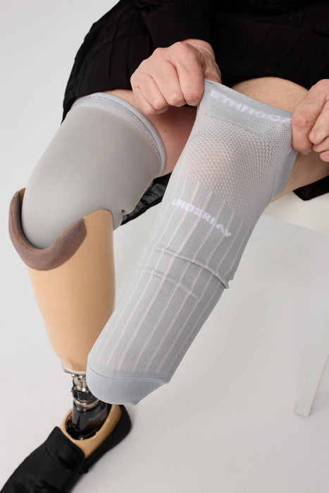 A close-up of a person putting on above their knee the Ethnocare Underlay Transtibial Closed Prosthetic Sweat Management Device around their residual limb. 