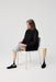Person seated against a white studio background, wearing a Ethnocare Underlay Transtibial Closed Prosthetic Sweat Management Device around their residual limb.