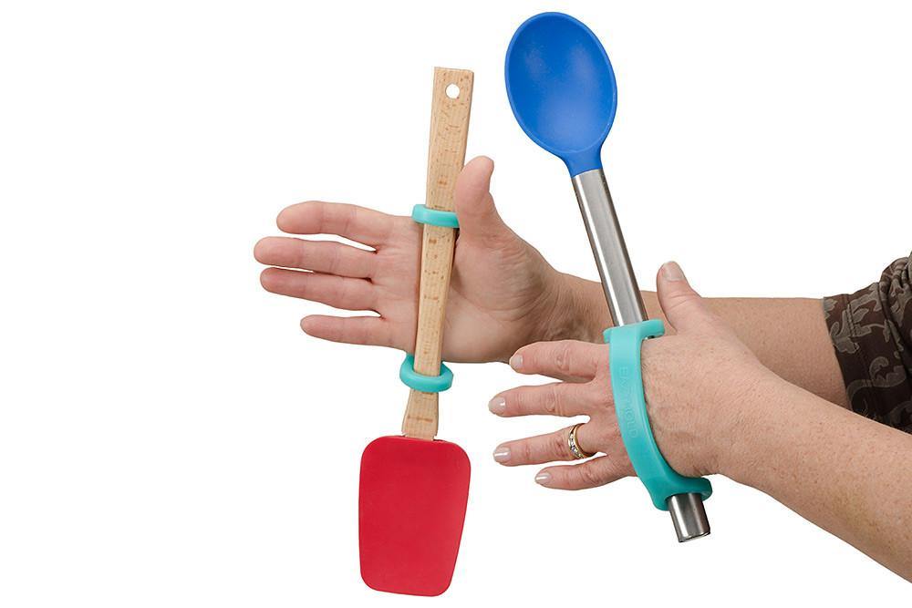 Hand holding a red spatula and blue spoon with an aqua EaZyHold Grip Aid on a white background
