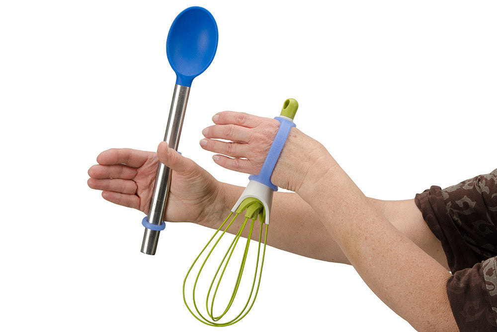Hand holding a blue spoon and green whisk with an EaZyHold Grid Aid on a white background