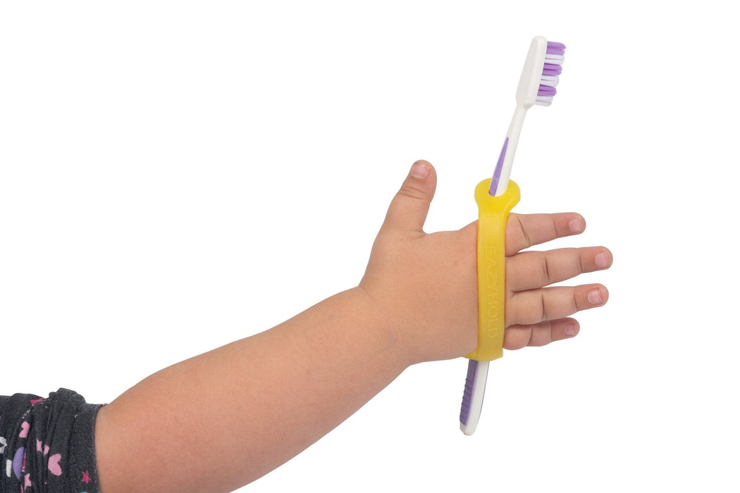 Hand holding a toothbrush with a yellow EaZyHold Grip Aid on a white background