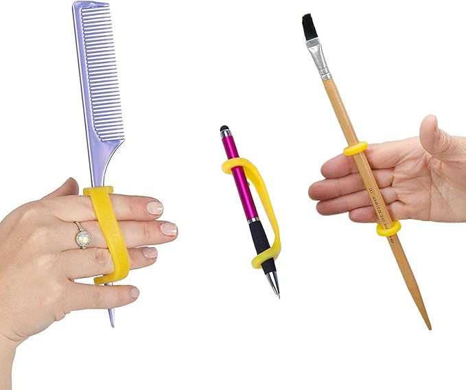 Hands holding a comb, pen, and paintbrush with a yellow EaZyHold Grip Aid on a white background
