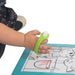 Child's hand holding a marker with a lime green EaZyHold Grip Aid over a coloring book with cartoon characters on a white background