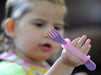 Child's hand holding a purple fork with an EaZyHold Grip Aid