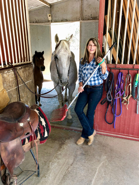 Woman standing with a horse in a stable holding a broom with an aqua EaZyHold Grip Aid