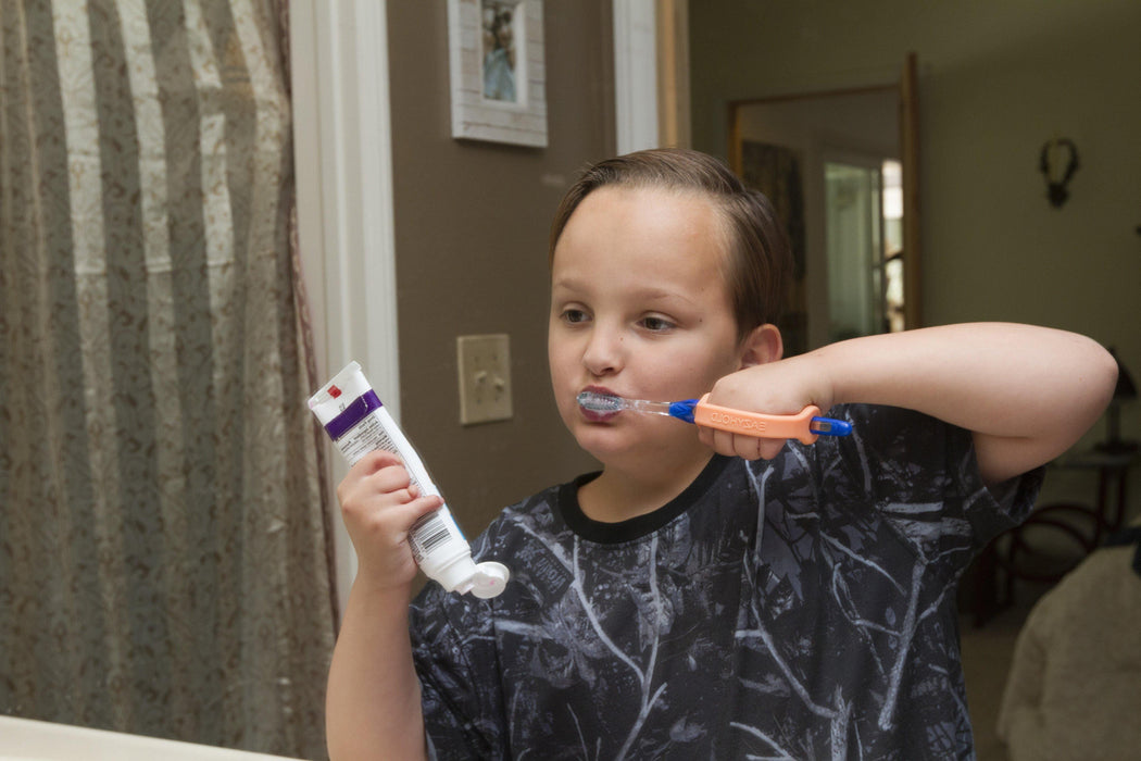 Child brushing teeth with an orange EaZyHold Grid Aid in a bathroom