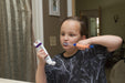 Child brushing teeth with an orange EaZyHold Grid Aid in a bathroom