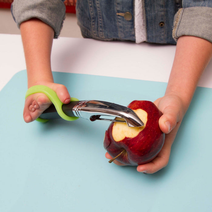 Person using an apple peeler with a green EaZyHold Grip Aid to remove skin from an apple on a light blue surface