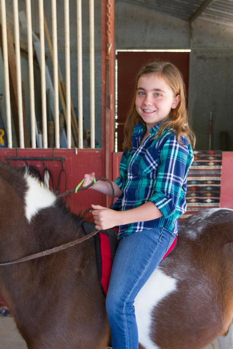 Girl sitting on a horse in a stable holding the reins with a green EaZyHold Grip Aid