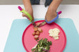 Child using colorful plastic utensils with an EaZyHold Grip Aid  to cut food on a pink plate