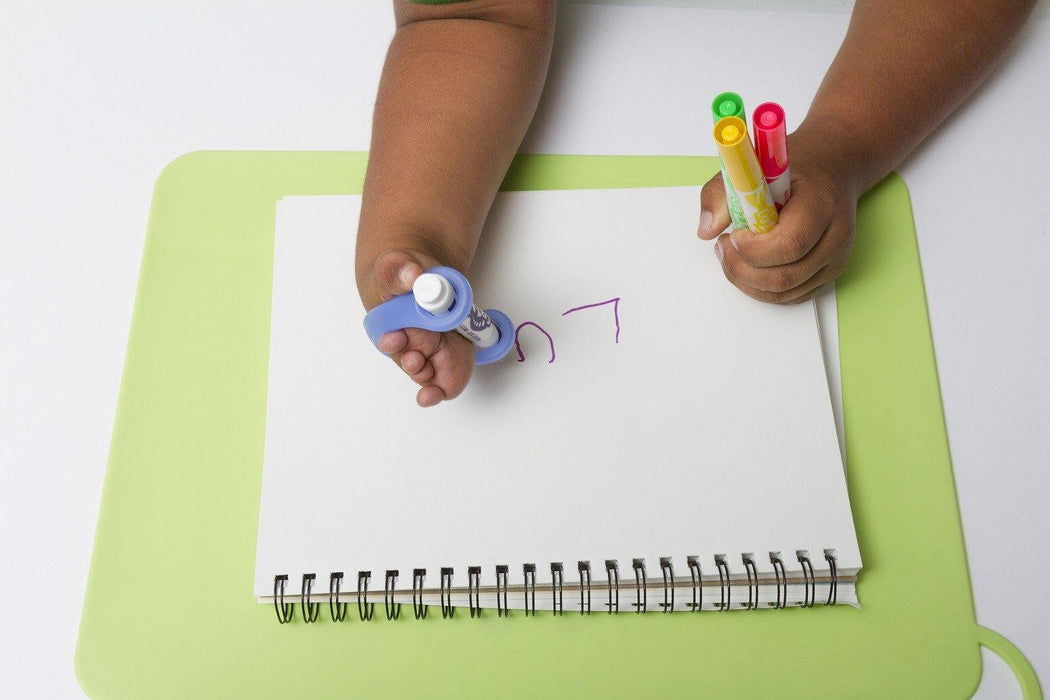 Child's writing on a notebook with a blue EaZyHold Grid Aid on a green surface