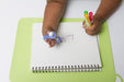 Child's writing on a notebook with a blue EaZyHold Grid Aid on a green surface