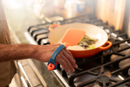 Person cooking on a gas stove with a pan and spatula, using an EaZyHold.