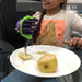 Child with a prosthetic hand holding a pear and a knife with a green EaZyHold Grip Aid on a plate