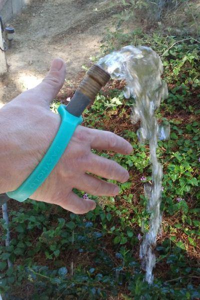 Hand holding a garden hose with water spraying out with an aqua EaZyHold Grip Aid outdoors