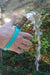 Hand holding a garden hose with water spraying out with an aqua EaZyHold Grip Aid outdoors
